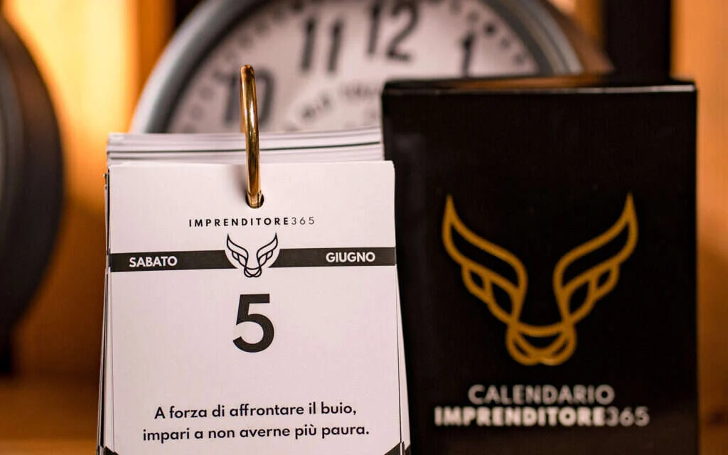 Calendario Imprenditore365 aperto su una frase di giugno accanto alla scatola nera e oro